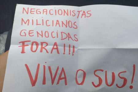 Psicóloga é impedida de receber a vacina em Porto Alegre segurando cartaz com palavras de protesto