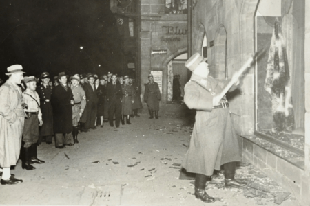 Pessoas observam oficial nazista atacar loja de um judeu na 